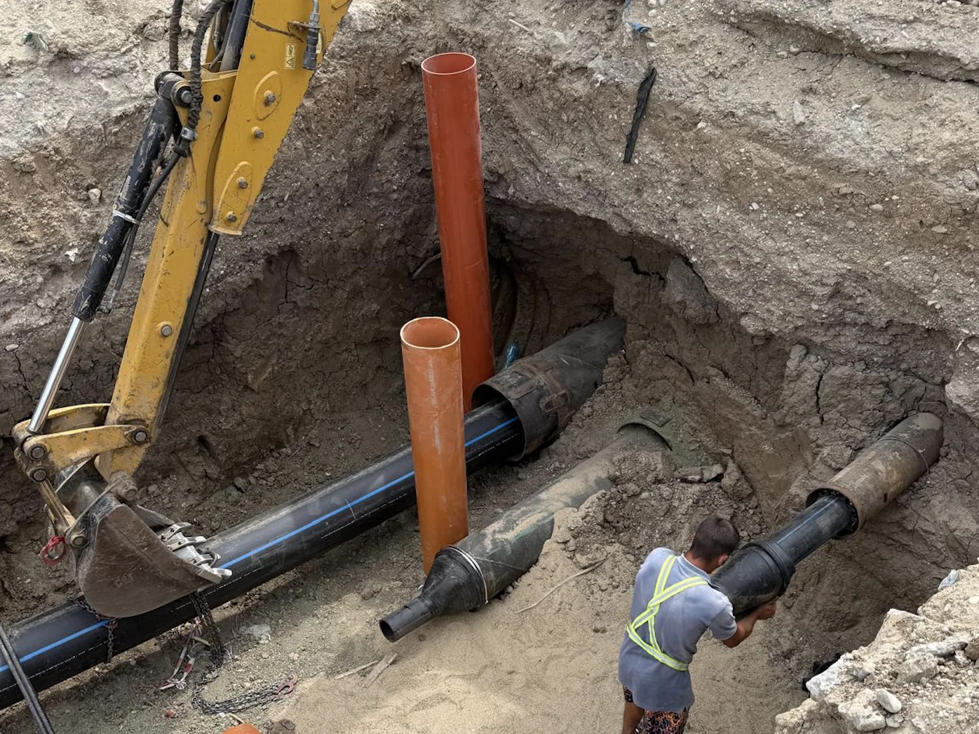 Subtraversare — pozare conductă în săpătură cu excavator și conducte portocalii